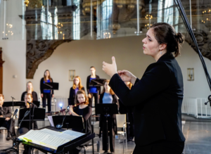vrouw dirigeert orkest en koor in kerk